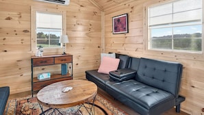 Ein gemütliches Blockhauss-Interieur mit einer Ledersofa, einem kleinen runden Tisch, einer Kommode und einem Fenster mit Aussicht.