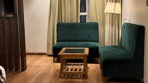 A living room with a green sofa, a wooden coffee table, a lamp, and a TV on the wall.