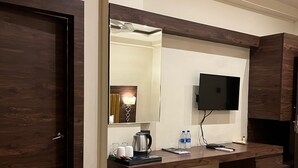 A hotel room with a wooden floor, a desk with a flat-screen TV, a coffee maker, and a trash bin.