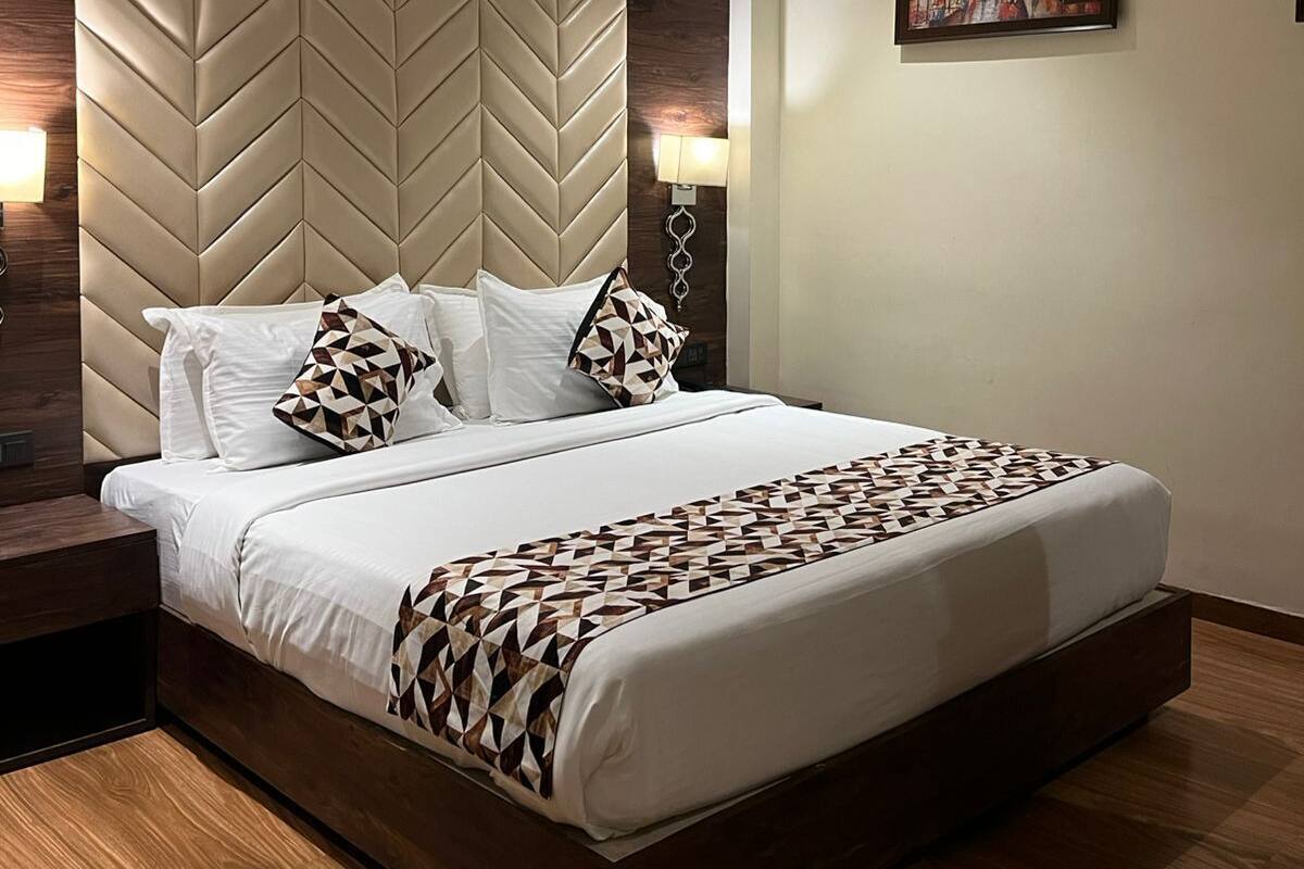 Una habitación de hotel moderna con una cama grande, un cabecero de madera, un cuadro en la pared y una mesita de noche con una lámpara.