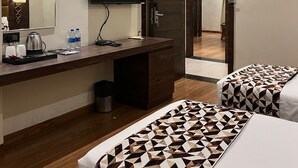 A hotel room with a desk, a flat-screen TV, two beds with patterned bedding, a mirror, and a door leading to another room.