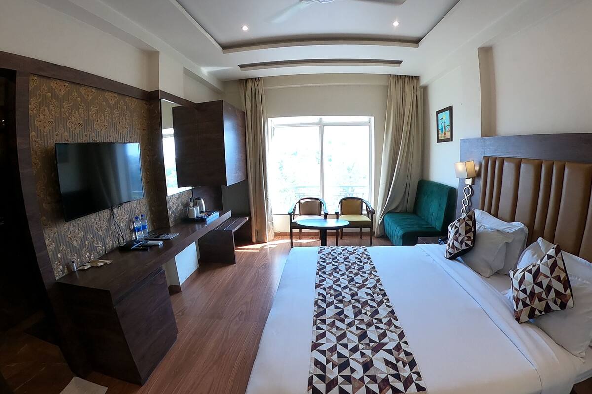 Habitación de hotel con una cama grande, un escritorio con televisor de pantalla plana, una zona de estar con sillas y vistas al exterior a través de un ventanal amplio.