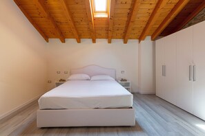 Ein Schlafzimmer mit Holzboden, einem Bett, einem Nachttisch, einem Kleiderschrank und einem Oberlicht.