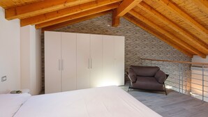 Une chambre avec un plafond en pente, un lit, une armoire, une chaise et un mur en pierre.