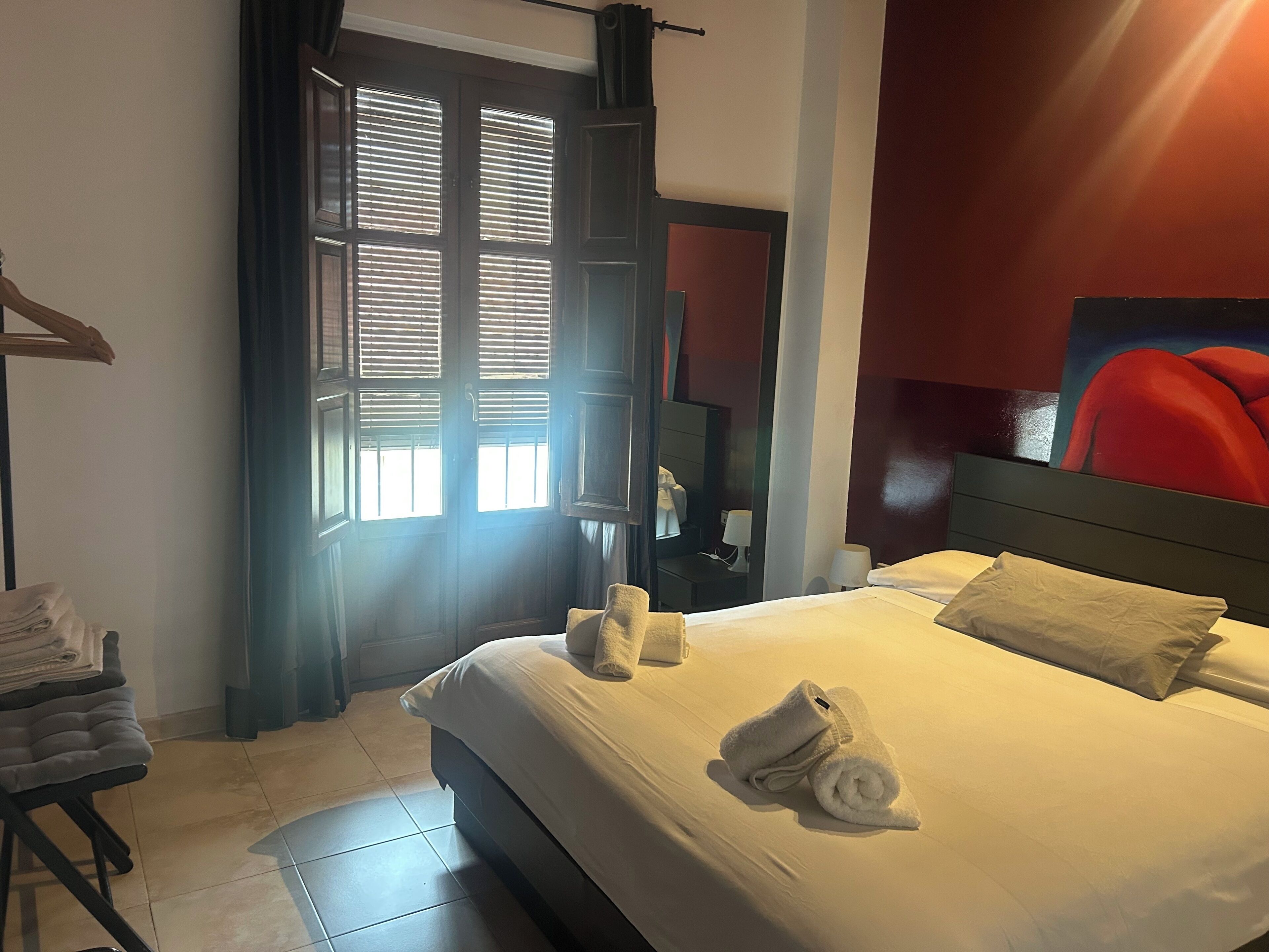 Ein Hotelzimmer mit Bett, Handtüchern, einem Nachttisch, einem Spiegel und einem Fenster mit Jalousien.