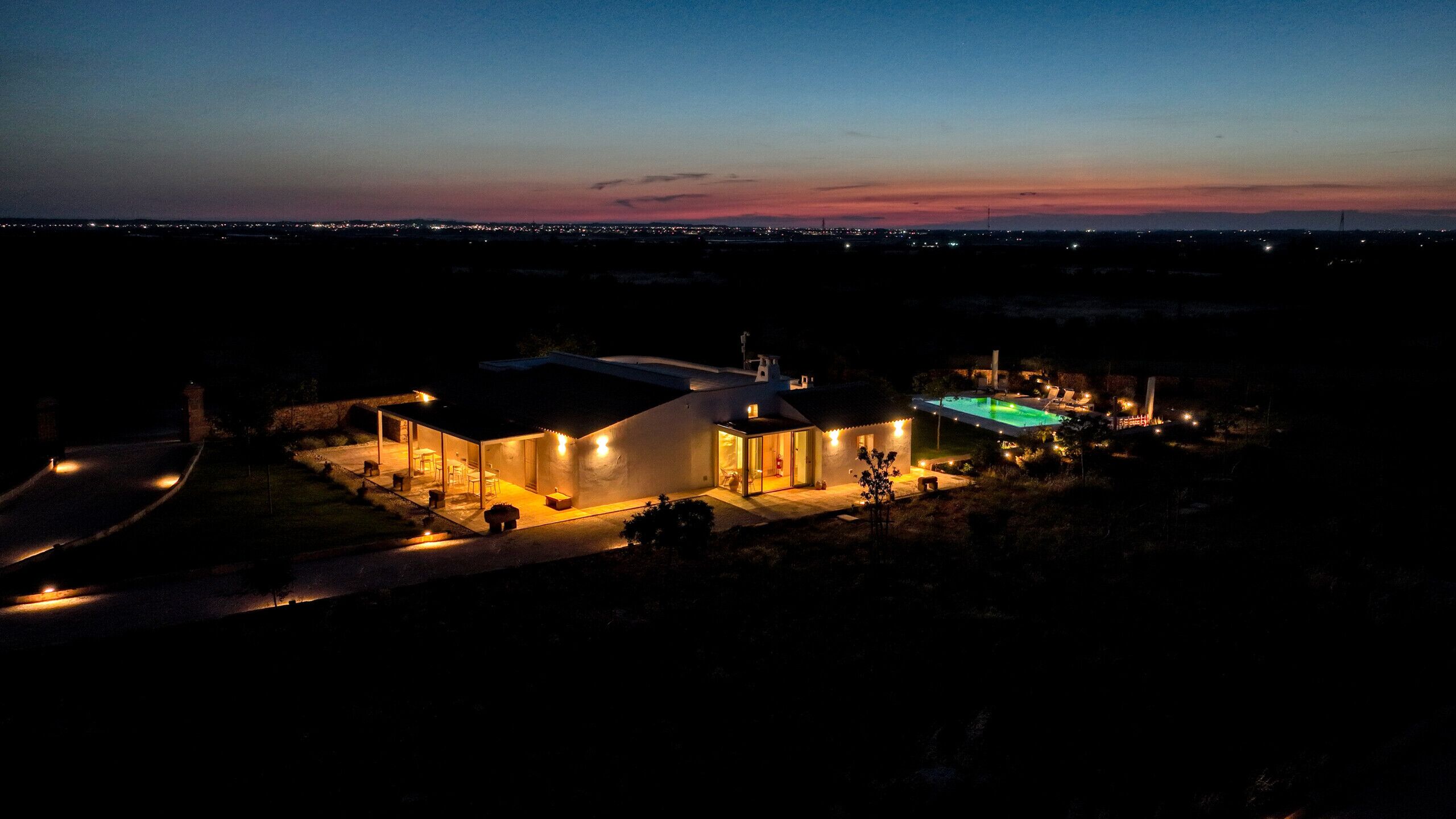 A modern house with a swimming pool, large windows, and a well-lit exterior at dusk.