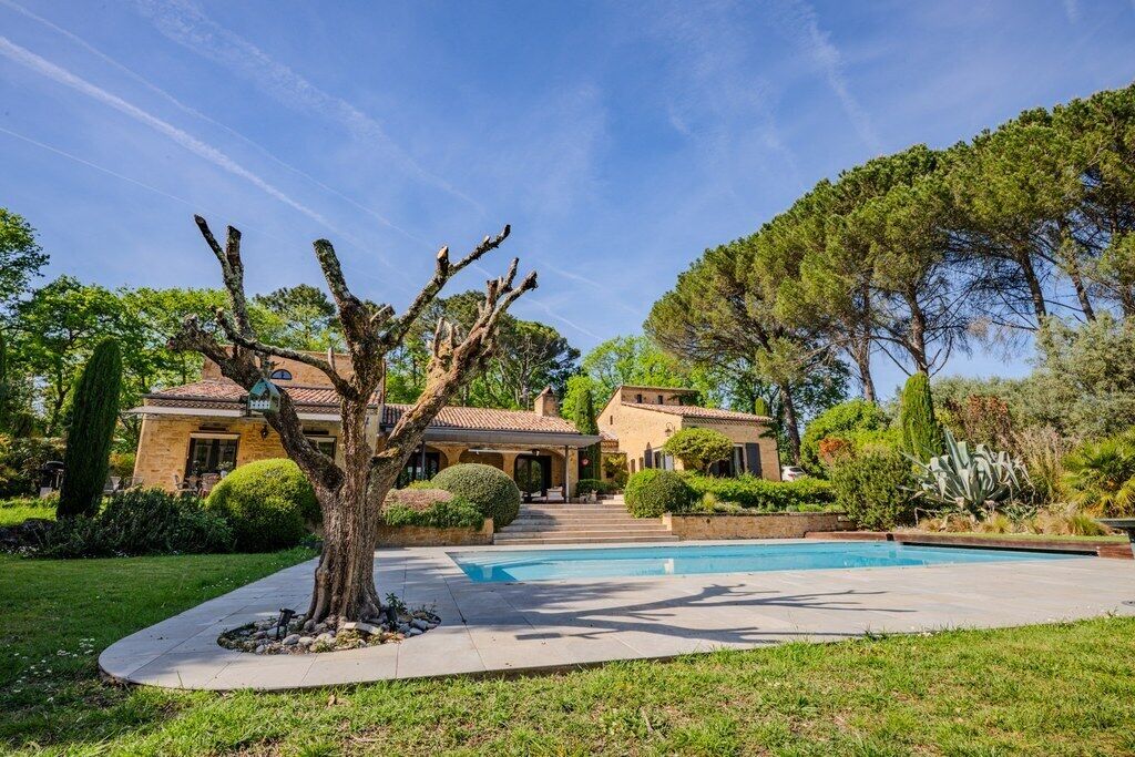 A house with a swimming pool, surrounded by well-maintained lawns and trees.