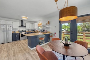 A modern kitchen with a central island, stainless steel appliances, and a dining area with a round table and chairs. - Convenient 3BD w/ Hot Tub | Huge Yard + Near TOWN! (Sevierville)