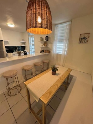 A modern kitchen with a wooden dining table, bar stools, and a woven light fixture.