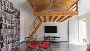 A modern interior with a wooden ceiling, a wall-mounted TV, a staircase, and a seating area with red cushions.