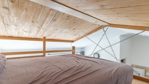 A bedroom with a wooden ceiling, a bed with a brown mattress, and a hanging chair.