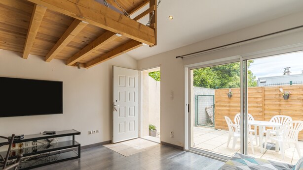 A spacious living area with a wooden ceiling, a sliding glass door leading to an outdoor patio, a flat-screen TV, and a sofa.