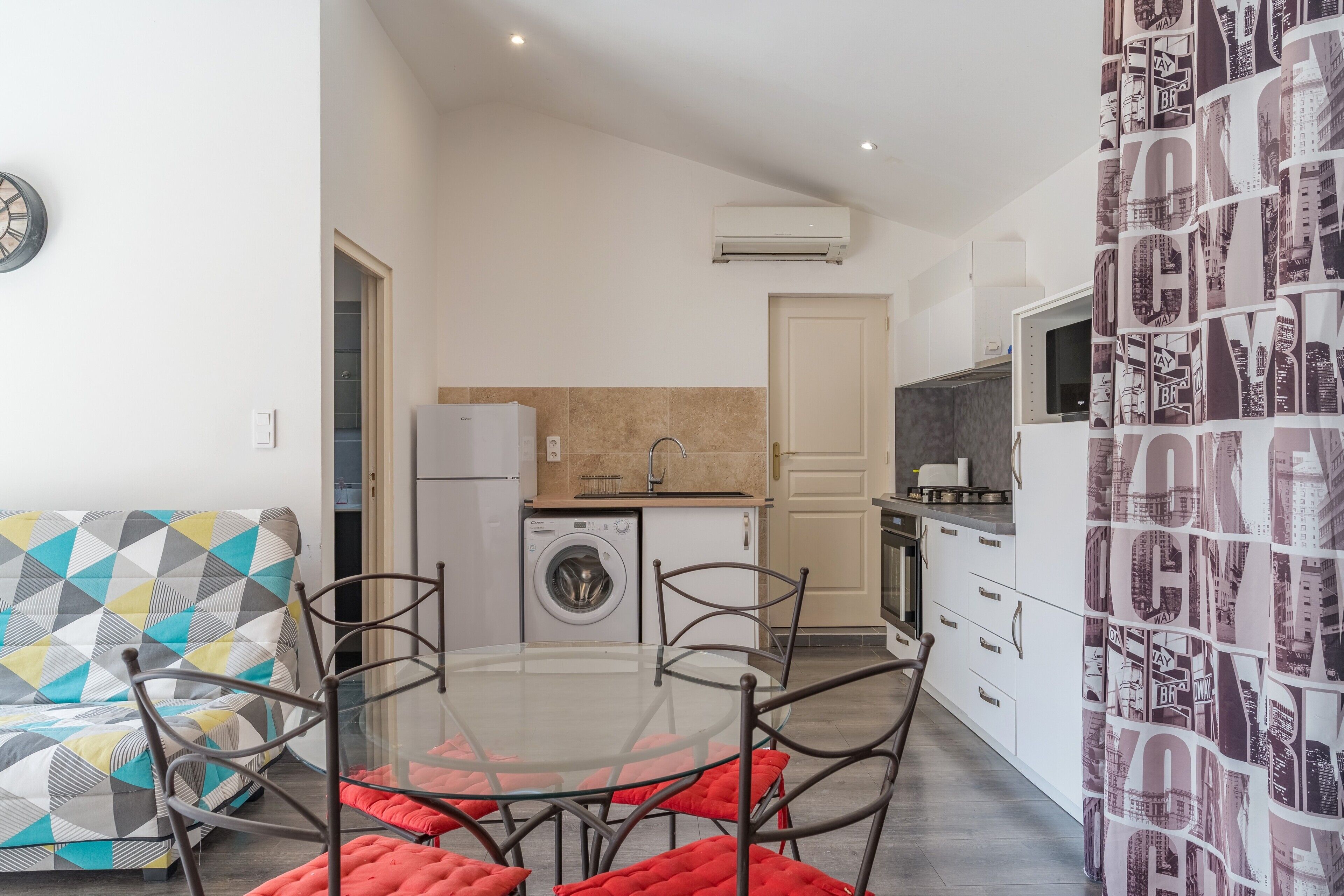 A modern kitchen with a washing machine, a dining table with chairs, and a sofa.