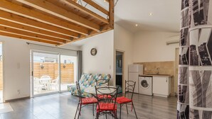 A modern kitchen with a washing machine, a dining area with red chairs, and a sofa with a geometric pattern.