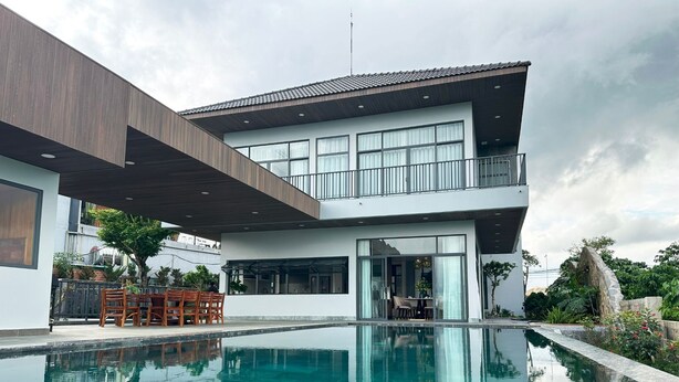 Una casa moderna de dos pisos con piscina, ventanas amplias y un balcón.
