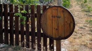 Une barrière en bois en forme de tonneau sur laquelle est inscrit le nom « Vino Ronja », une clôture en bois et un vignoble avec des rangs de vignes.