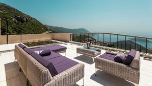 Une terrasse sur le toit, aménagée avec des meubles en osier, une table en verre et offrant une vue sur la mer.