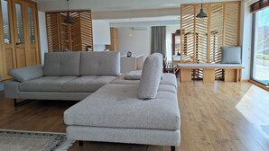 Un salon moderne avec un canapé d’angle gris, un banc en bois et une grande fenêtre laissant entrer la lumière naturelle.