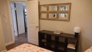 A bedroom with a bed, a nightstand with a lamp, a mirror, and a door leading to another room. - Exclusive 2-bdrm ocean & mountain view suite (Bowen Island)