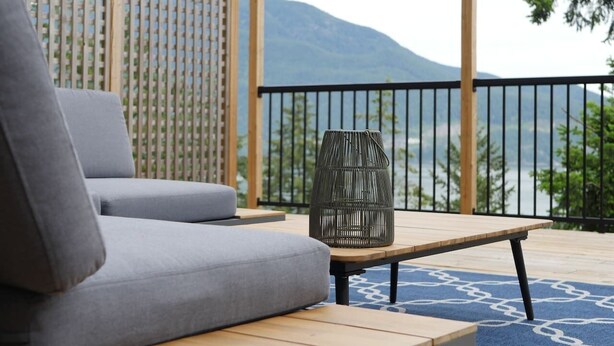 A balcony with a sofa, a wicker chair, and a view of a mountain. - Exclusive 2-bdrm ocean & mountain view suite (Bowen Island)