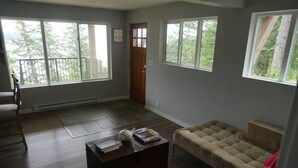 A living room with a sofa, a coffee table, and a door. - Exclusive 2-bdrm ocean & mountain view suite (Bowen Island)