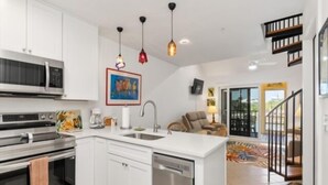 A modern kitchen with white cabinets, a dishwasher, and a microwave. There is a dining area with a chair and a table, and a staircase leading to another level. - Welcome to your slice of paradise on Little Gasparilla Island (Placida, Little Gasparilla Island)