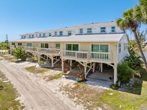 Ein Strandhotel mit mehreren Balkonen, einer Sandzufahrt und Palmen.