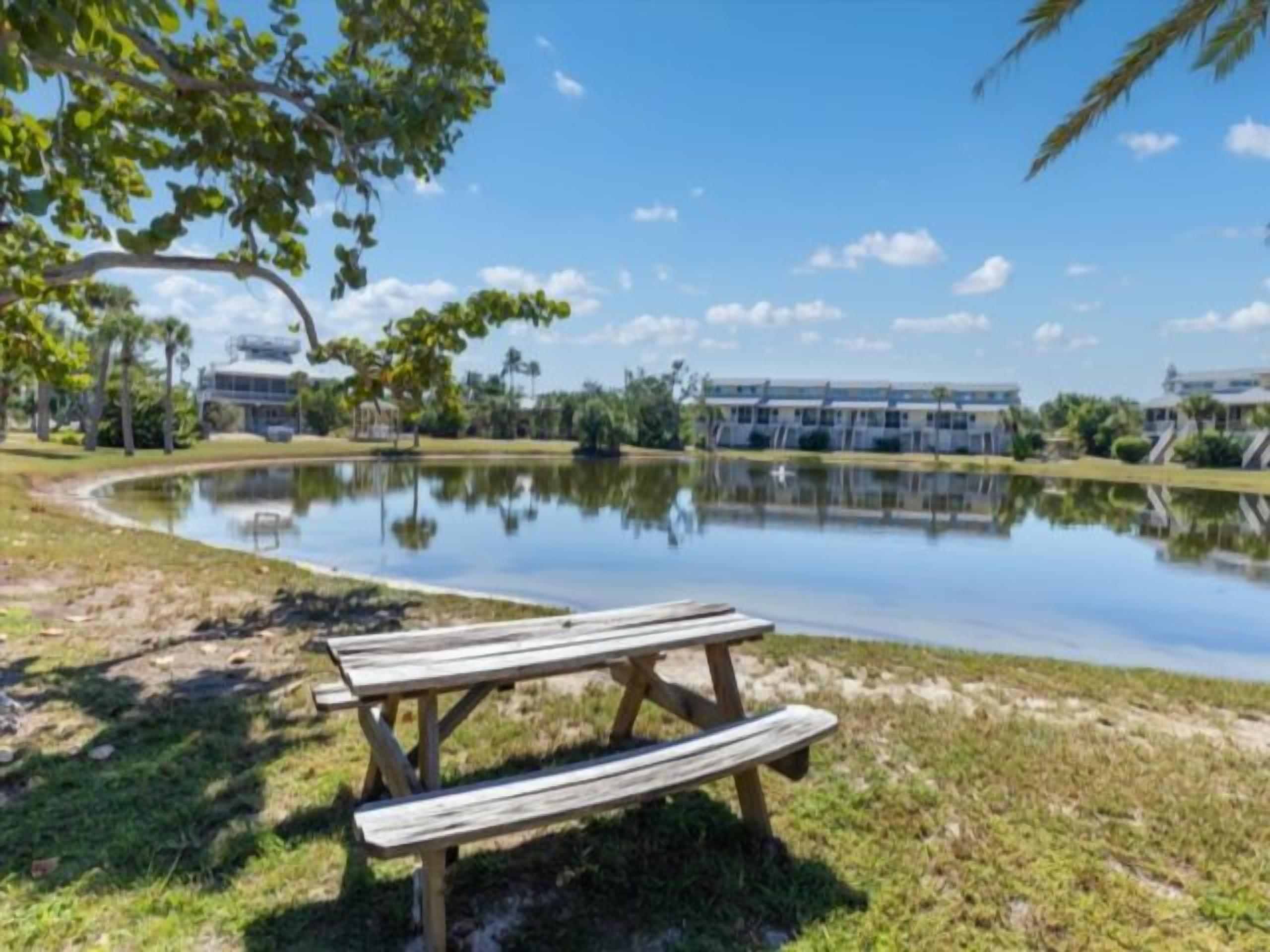 A picnic table by a calm pond with a clear sky.