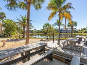 A wooden deck with picnic tables overlooking a calm body of water, surrounded by palm trees and greenery. - Welcome to your slice of paradise on Little Gasparilla Island (Placida, Little Gasparilla Island)