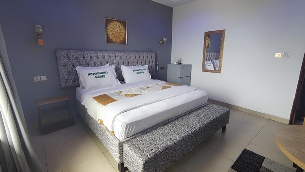 A neatly arranged hotel room with a bed, bedside tables, a mirror, and a small table. - Hôtel Résidence Segmad de Kribi (Kribi)