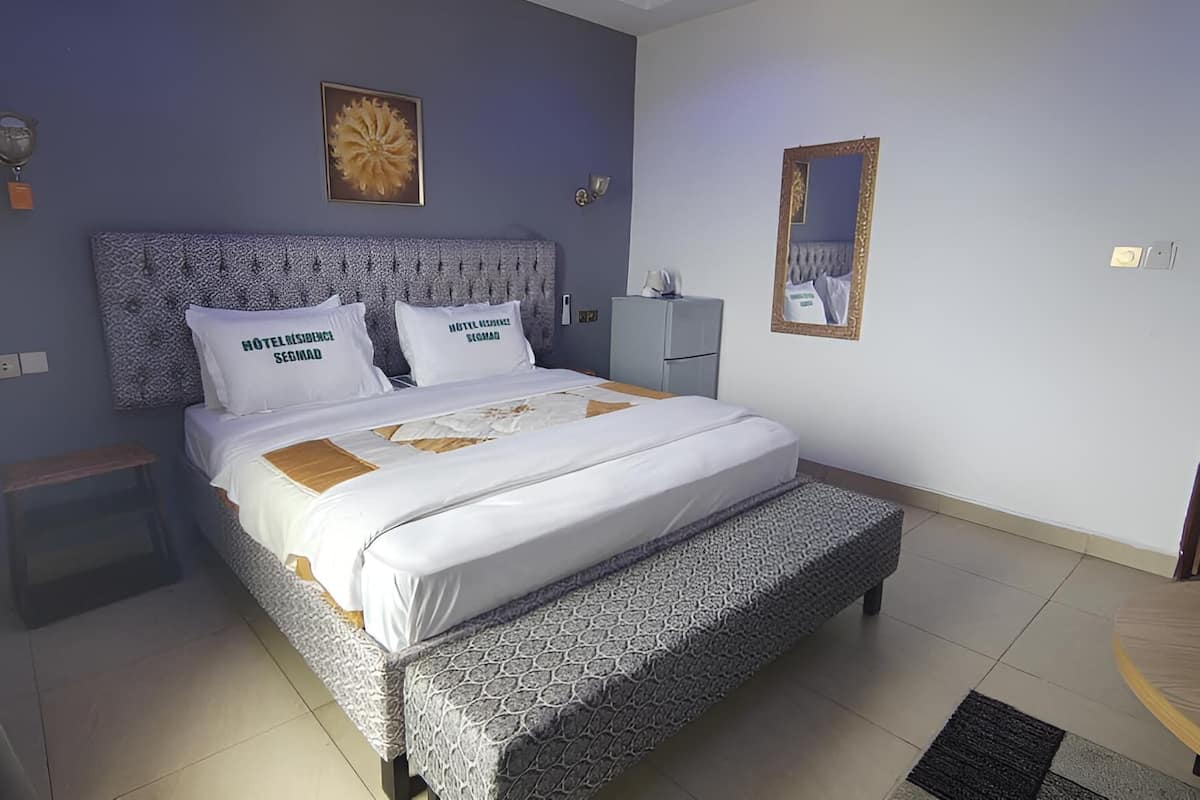 Ein ordentlich eingerichtetes Hotelzimmer mit Bett, Nachttischen, einem Spiegel und einem kleinen Tisch.
