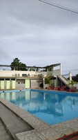Una piscina con una zona techada, escaleras y un edificio con balcón.