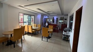 A dining area with yellow chairs and tables, a bar area with shelves of bottles, and a view of the street outside. - Hôtel Résidence Segmad de Kribi (Kribi)