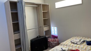 Ein Schlafzimmer mit Kleiderschrank, einem Bett mit geometrischem Muster auf der Bettdecke, einem Koffer und einer Tasche.