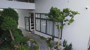 A modern building with a glass door entrance, a pathway, and a small garden with rocks and plants. - BB HOUSE: VILLA SANG TRỌNG TẠI BẢO LỘC (3 Bảo Lộc)