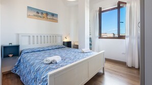 Ett sovrum med en säng, ett nattduksbord, en lampa, en tavla och ett fönster med gardiner.
