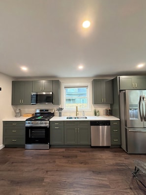 A modern kitchen with dark green cabinets, stainless steel appliances, and a window with a view of the outside.