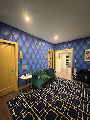 A room with a green sofa, a patterned rug, and a blue wall.