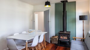 A dining area with a white table and chairs, a black hanging light, a green wall, and a wood-burning stove. - Central Taupo Getaway by Aotearoa Escapes (Taupo)
