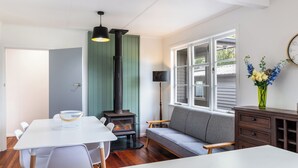 A room with a white table, a gray sofa, a wooden cabinet, a black lamp, a green wall, and a window with a clock. - Central Taupo Getaway by Aotearoa Escapes (Taupo)