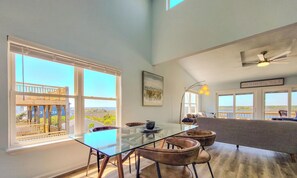A spacious room with a glass dining table, leather chairs, a sofa, and a ceiling fan. - The Sandcastle: Renovated + Ready for You (Surf City)