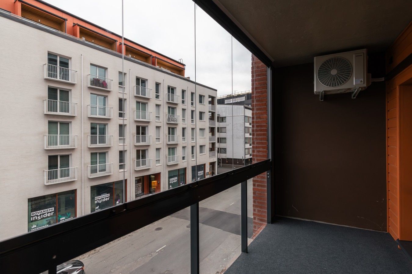 A balcony with a view of a multi-story building, an air conditioning unit, and a door.