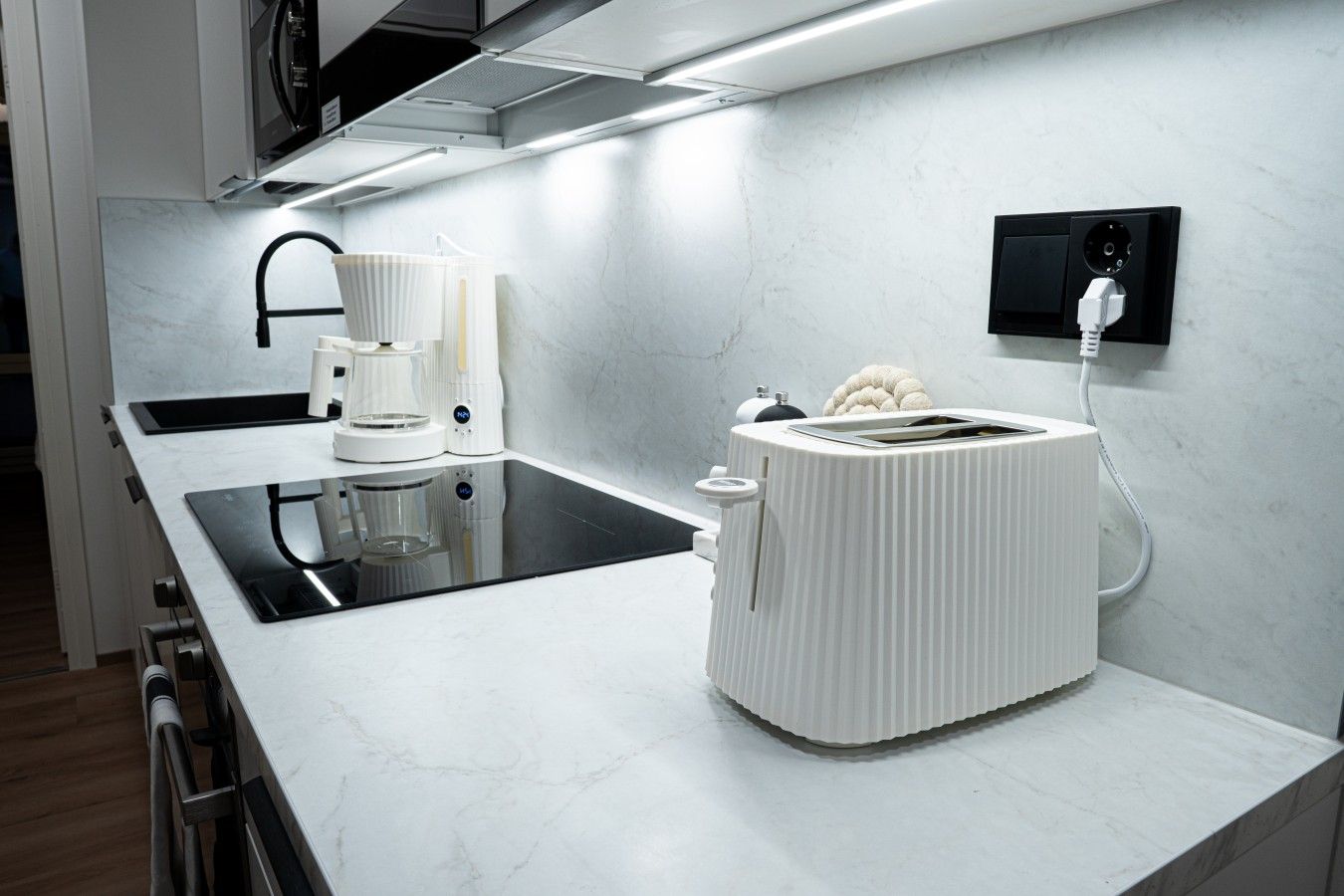 Eine moderne Küche mit weißer Arbeitsplatte, integriertem Backofen, Kaffeemaschine und Toaster.