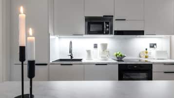 A modern kitchen with a built-in microwave, a sink, and a stove. There are candles on a stand, a coffee maker, and a bowl of green apples on the counter.