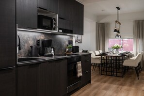 A modern kitchen with dark cabinetry, a built-in microwave, and a coffee maker. - Snownest Premium City Centre Apartments 2 (Rovaniemi)