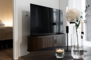 A modern living room with a flat-screen TV mounted on a wooden cabinet, a lit candle on a table, and a vase with flowers. - Snownest Premium City Centre Apartments 2 (Rovaniemi)