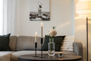 A round table with two candles and a vase with flowers, a sofa with cushions, and a lamp in a living room. - Snownest Premium City Centre Apartments 2 (Rovaniemi)