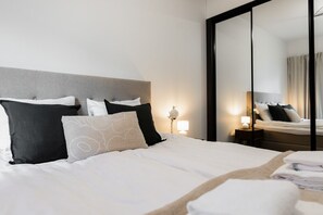 A neatly made bed with a grey headboard, white bedding, and several pillows in black and beige. - Snownest Premium City Centre Apartments 2 (Rovaniemi)