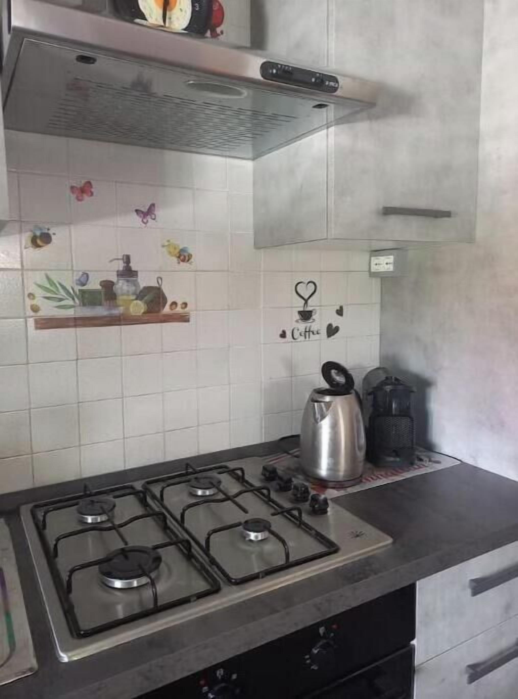 A kitchen with a gas stove, a kettle, and a coffee station.