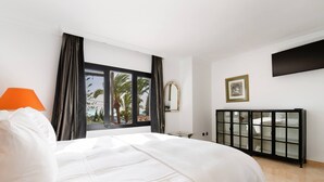 A hotel room with a bed, a window with curtains, a bedside table, a TV mounted on the wall, and a cabinet with glass doors. - 3310 Villa Flores (Marbella)
